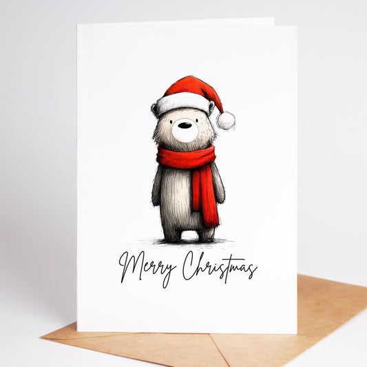 Bear Christmas card: a bear in a red Santa hat and scarf above Merry Christmas, standing on a kraft envelope
