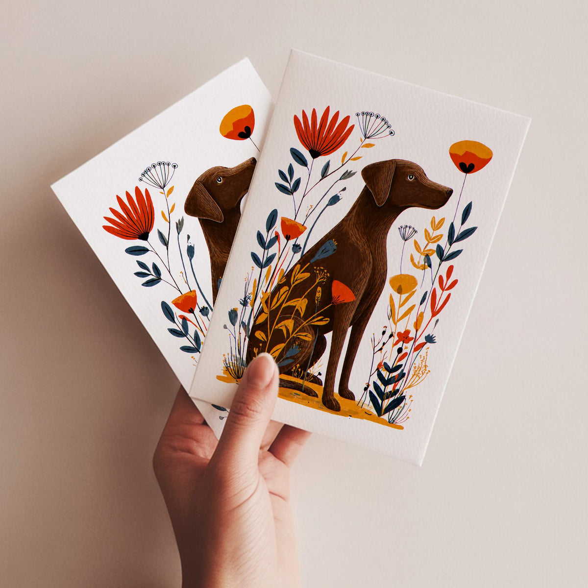 A hand holding two Chocolate Lab cards to show their A2 size