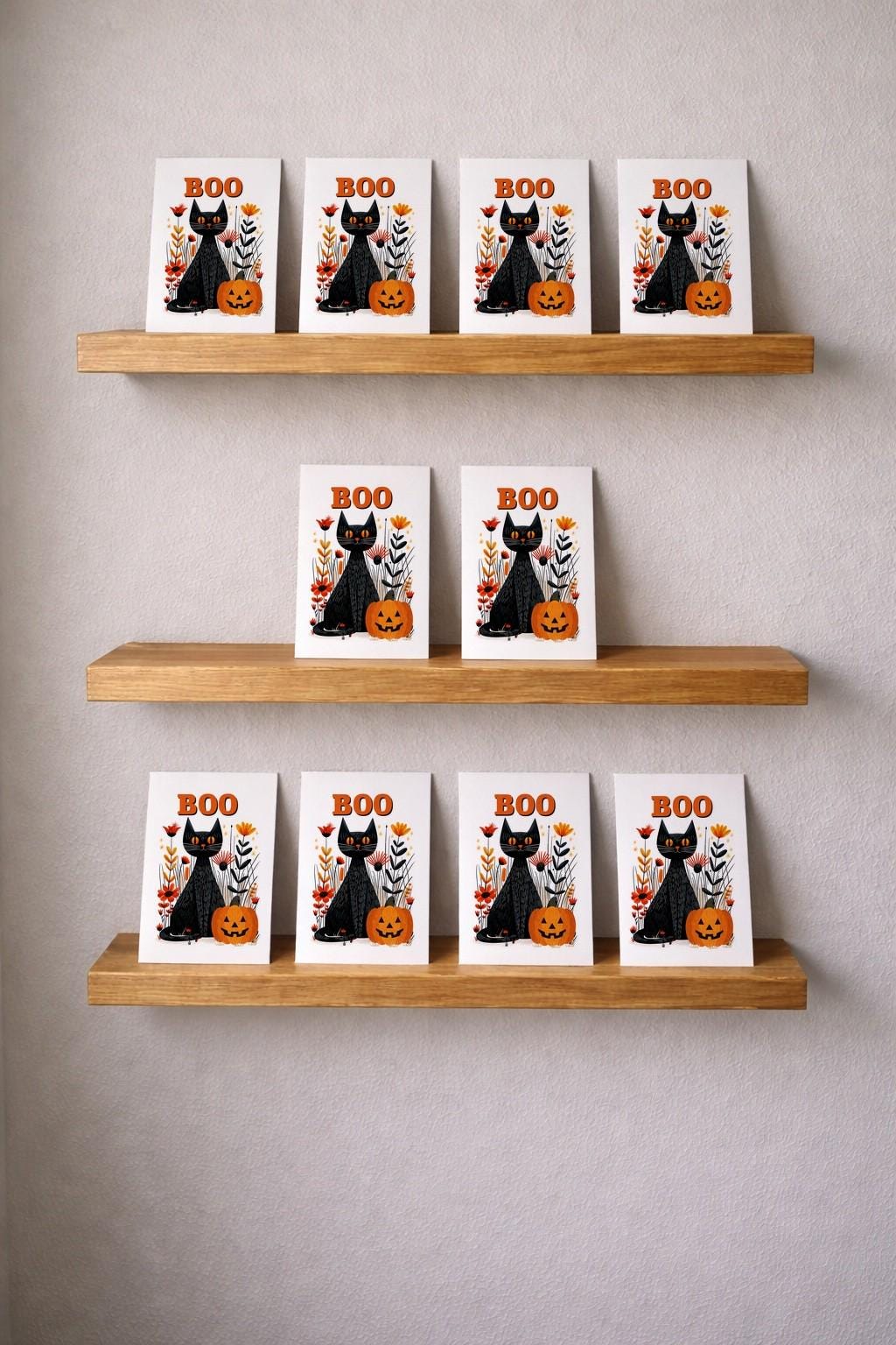 Twelve Boo black cat Halloween cards displayed on three wooden picture ledges against a grey wall