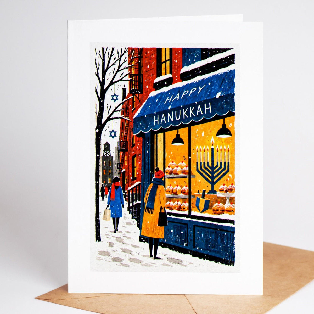 New York Hanukkah card standing upright, a bakery window of sufganiyot beside a lit menorah