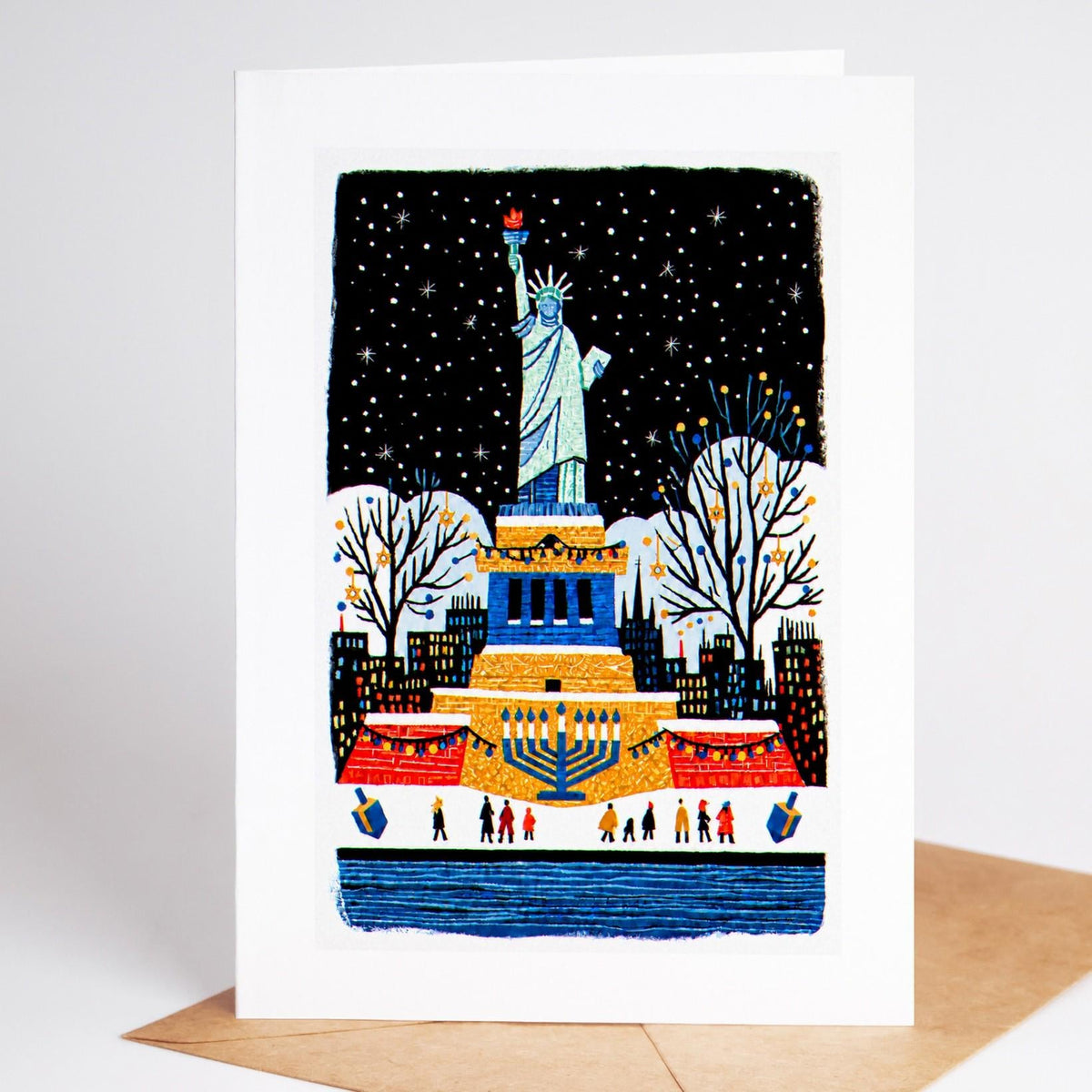 New York Hanukkah card standing upright, the Statue of Liberty above a lit menorah and dreidels