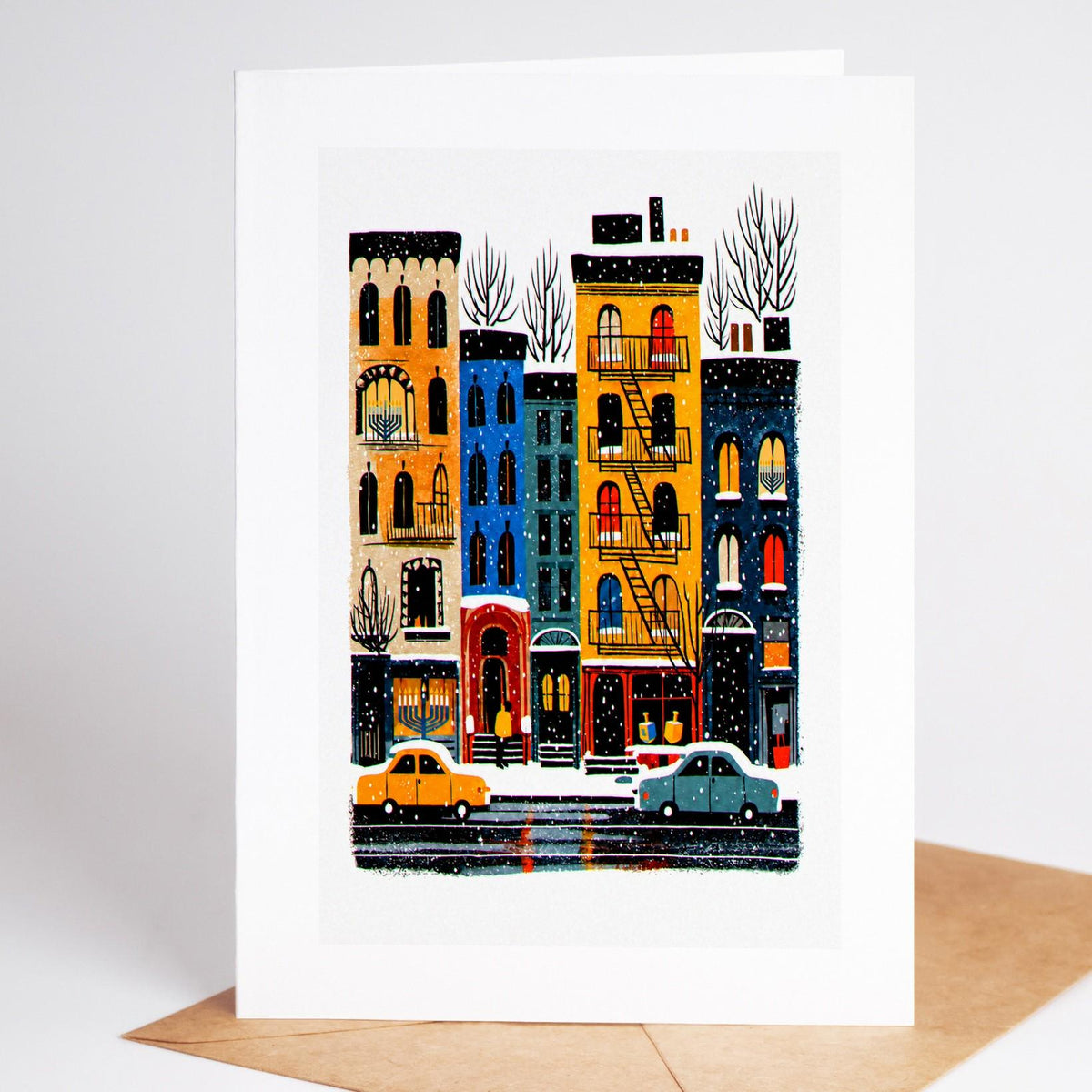 New York Hanukkah card standing upright, a block of brownstones at night with a lit menorah in an upper window