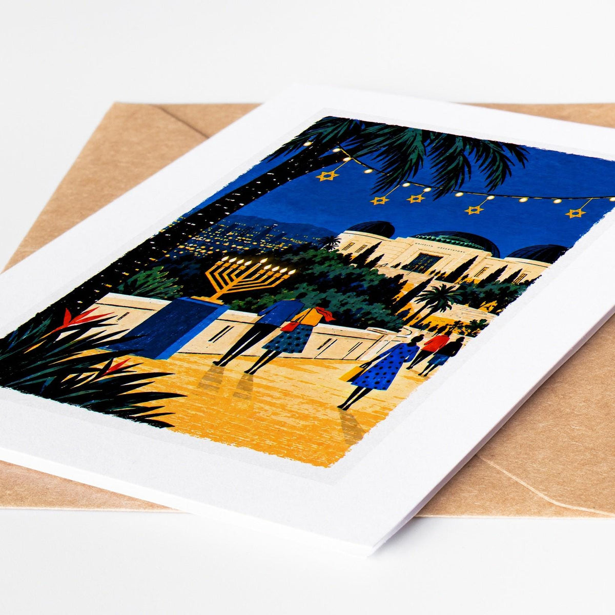 Los Angeles Hanukkah card lying on a kraft envelope, folk art Griffith Observatory above the city lights with a lit meno