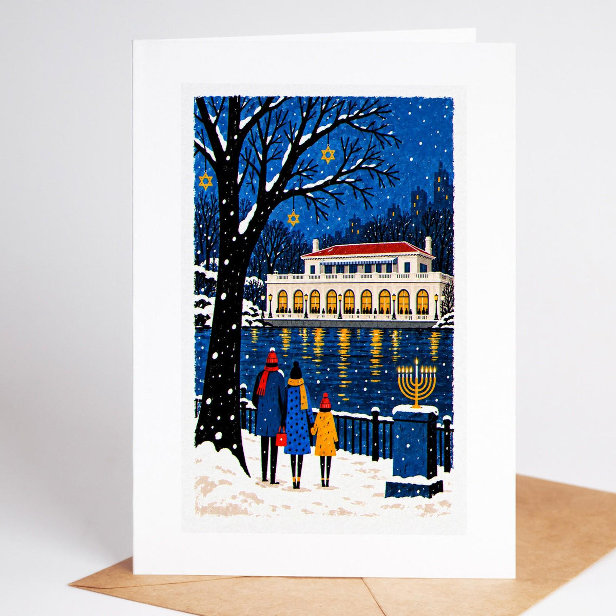 Brooklyn Hanukkah card standing with envelope, the Prospect Park boathouse lit at dusk with a menorah on the path