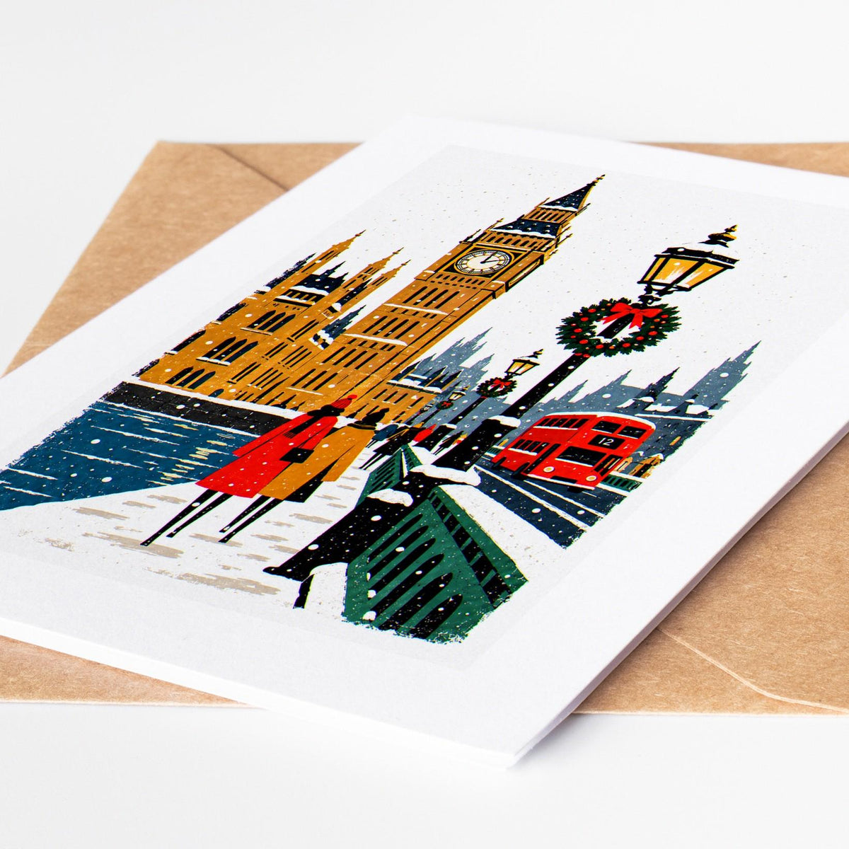 London Christmas card lying on a kraft envelope, folk art Big Ben and Westminster in the snow with a red double decker b