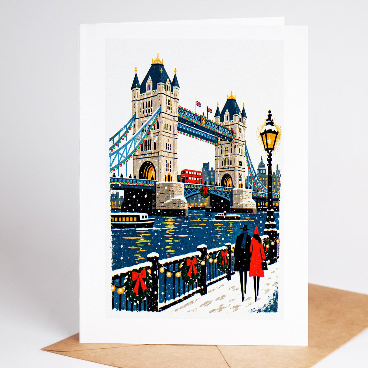 London Christmas card standing upright, Tower Bridge lit at night above the Thames in falling snow
