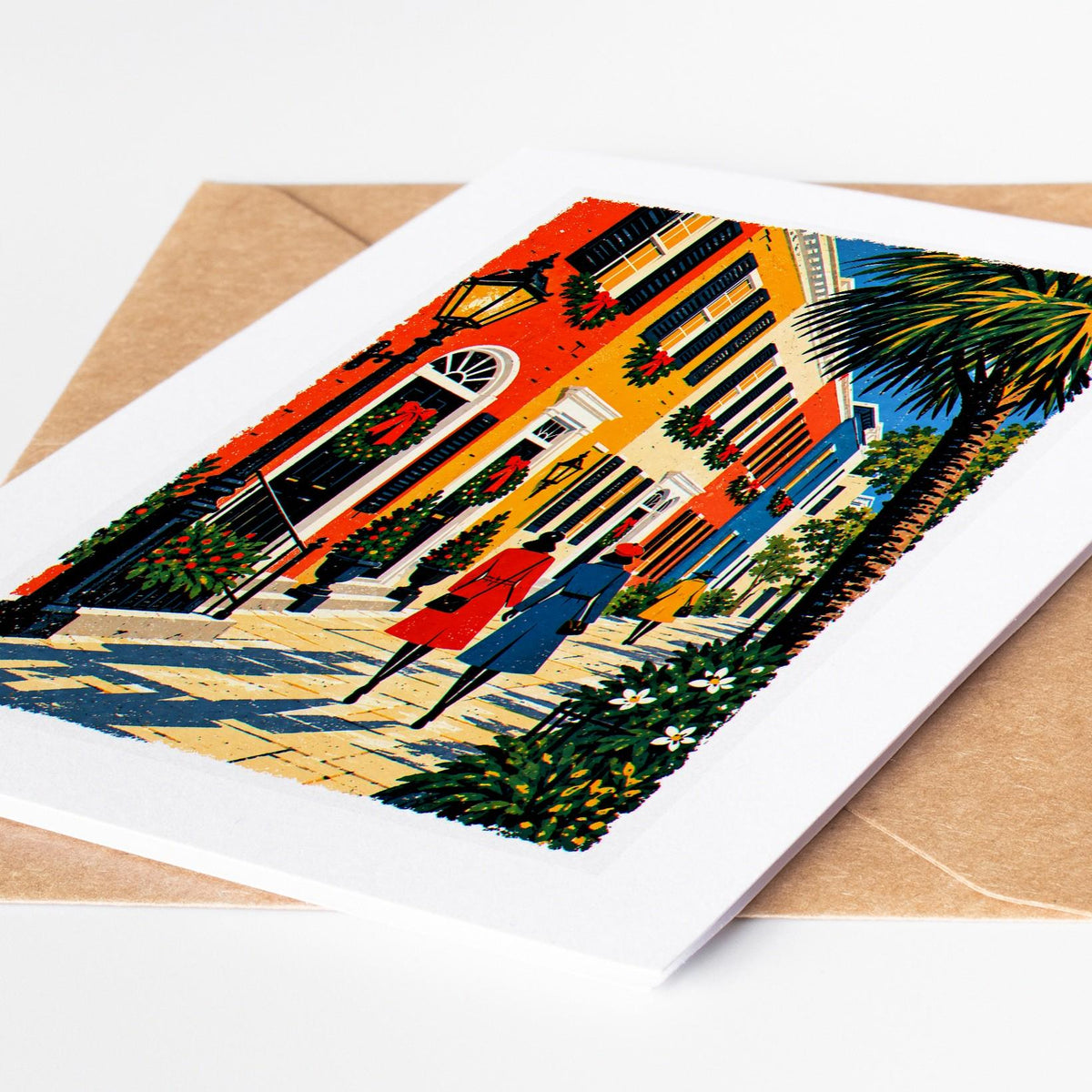 Charleston Christmas card lying on a kraft envelope, folk art Rainbow Row pastel houses decked in garlands and wreaths