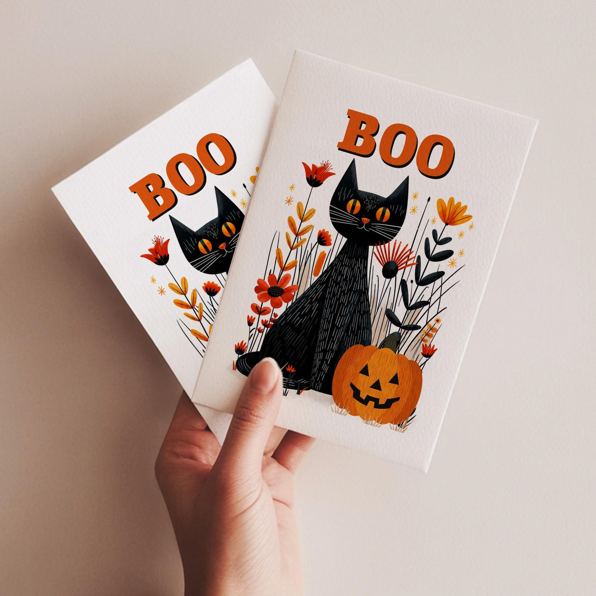 A hand holding two Boo black cat Halloween cards, folk art cat and jack-o-lantern