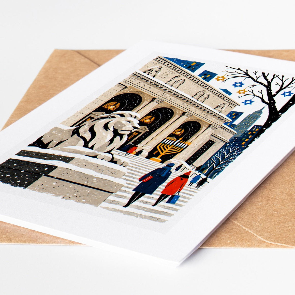 New York Hanukkah card lying on a kraft envelope, folk art library lions in the snow with a lit menorah on the steps