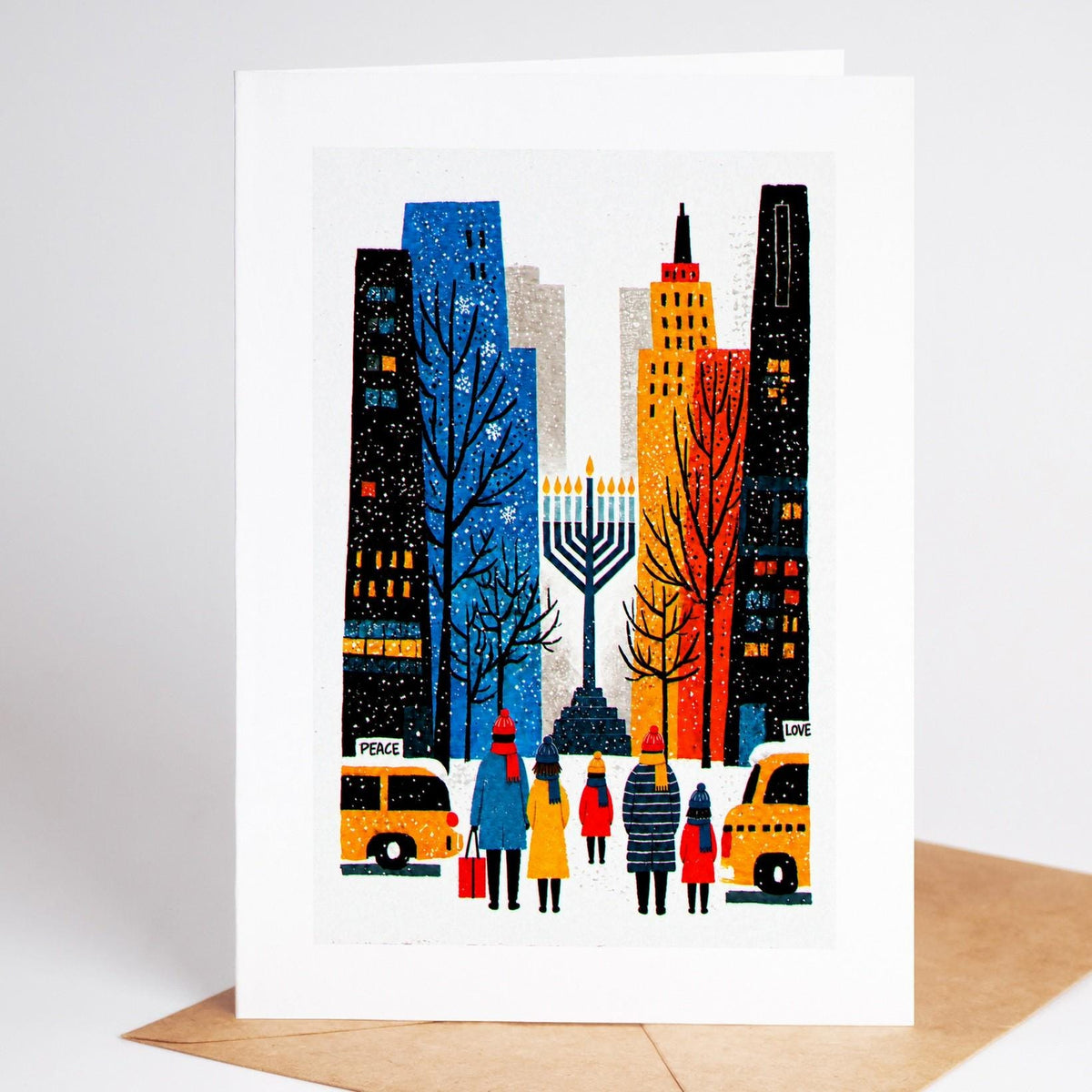 New York Hanukkah card standing with envelope, a large lit menorah in a city plaza between blue and gold buildings