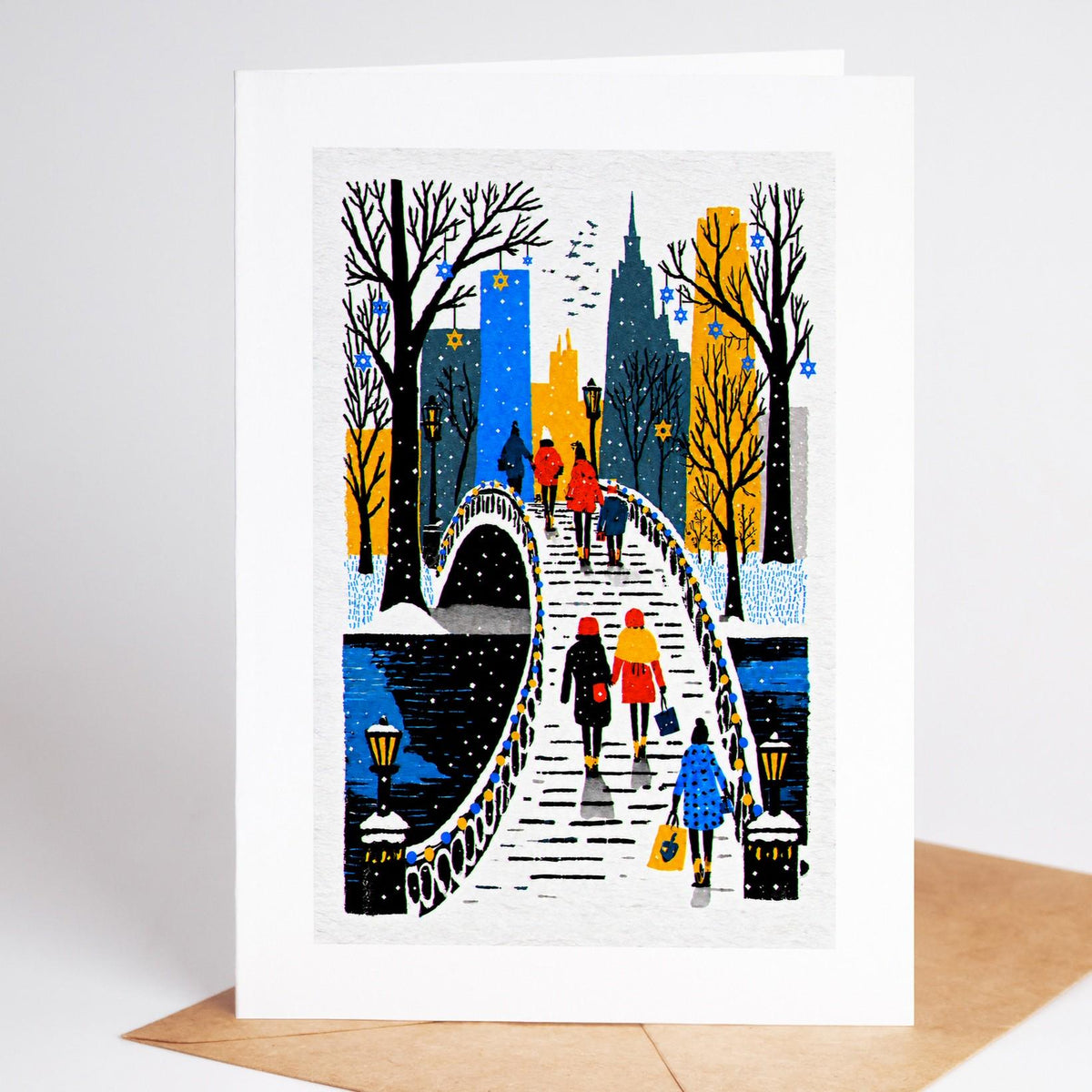 New York Hanukkah card standing with envelope, a lantern-lit park bridge in the snow hung with Stars of David
