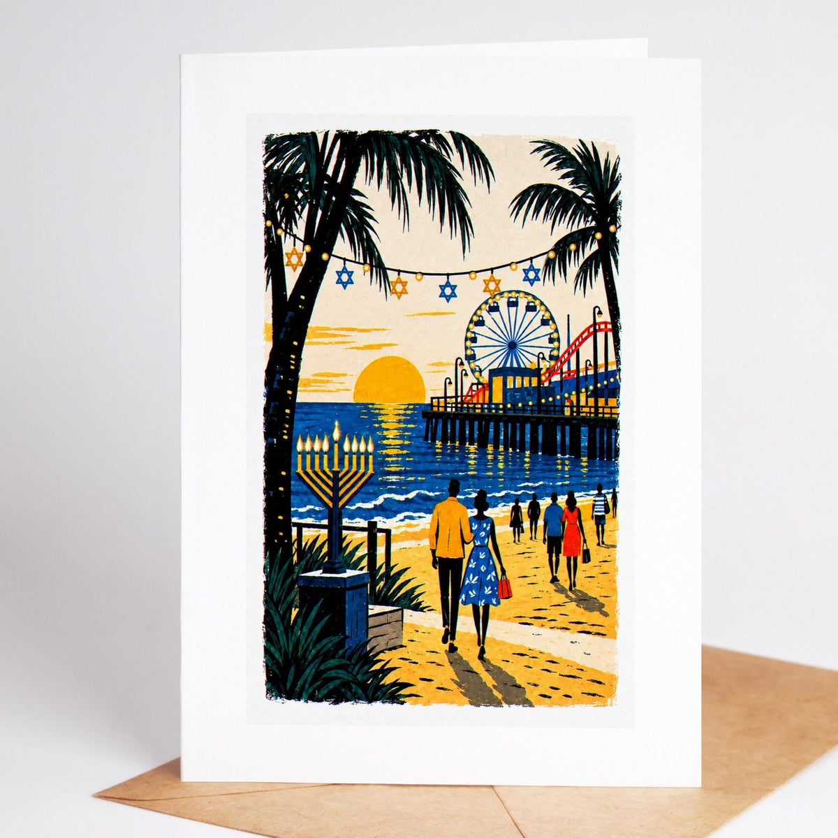 Los Angeles Hanukkah card standing upright, the Santa Monica Pier at sunset with a lit menorah on the sand